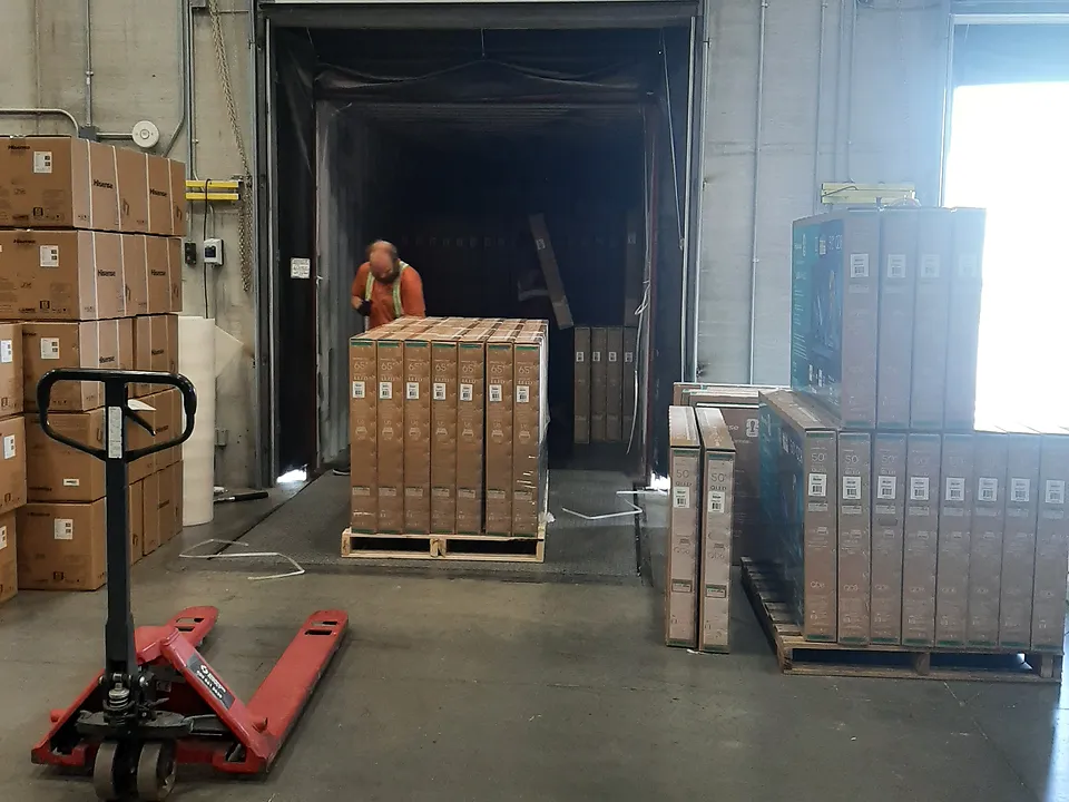 Open dock door with a pallet of cartons on the dock plate and a red hand pallet jack in front