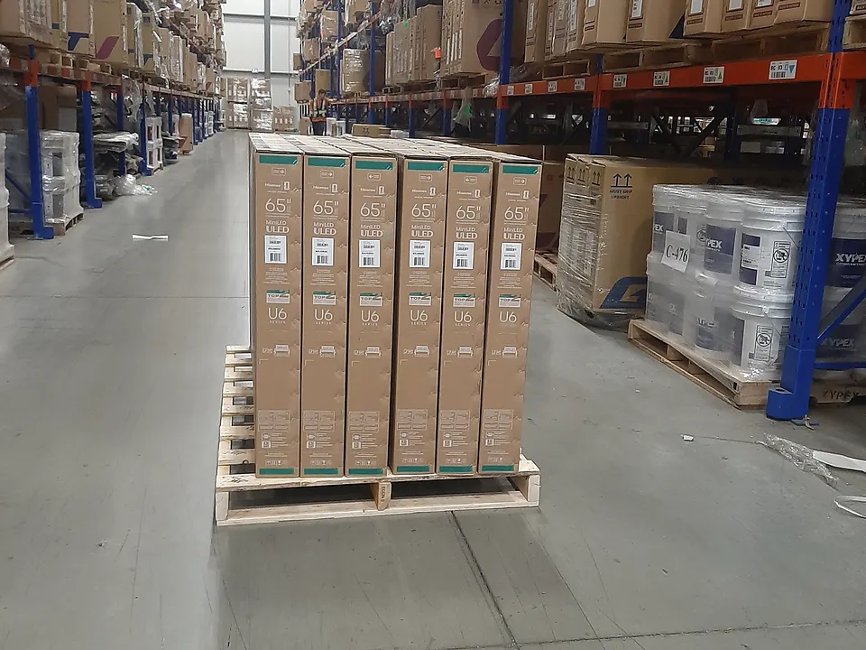 Single-product pallet of upright cartons on the floor of a racked warehouse aisle