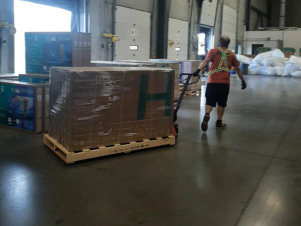 Crew member pulling a wrapped pallet away from the dock with a manual pallet jack, seen from behind