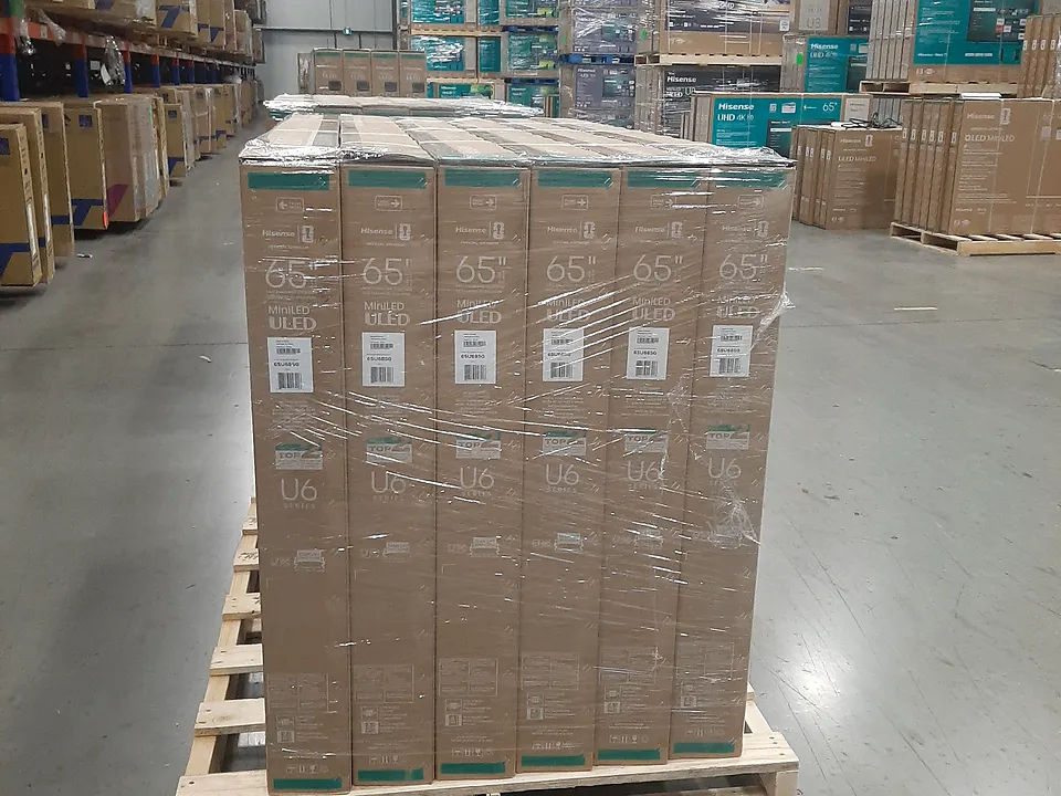 Stretch-wrapped pallet of tall, flat cartons standing upright in a warehouse aisle