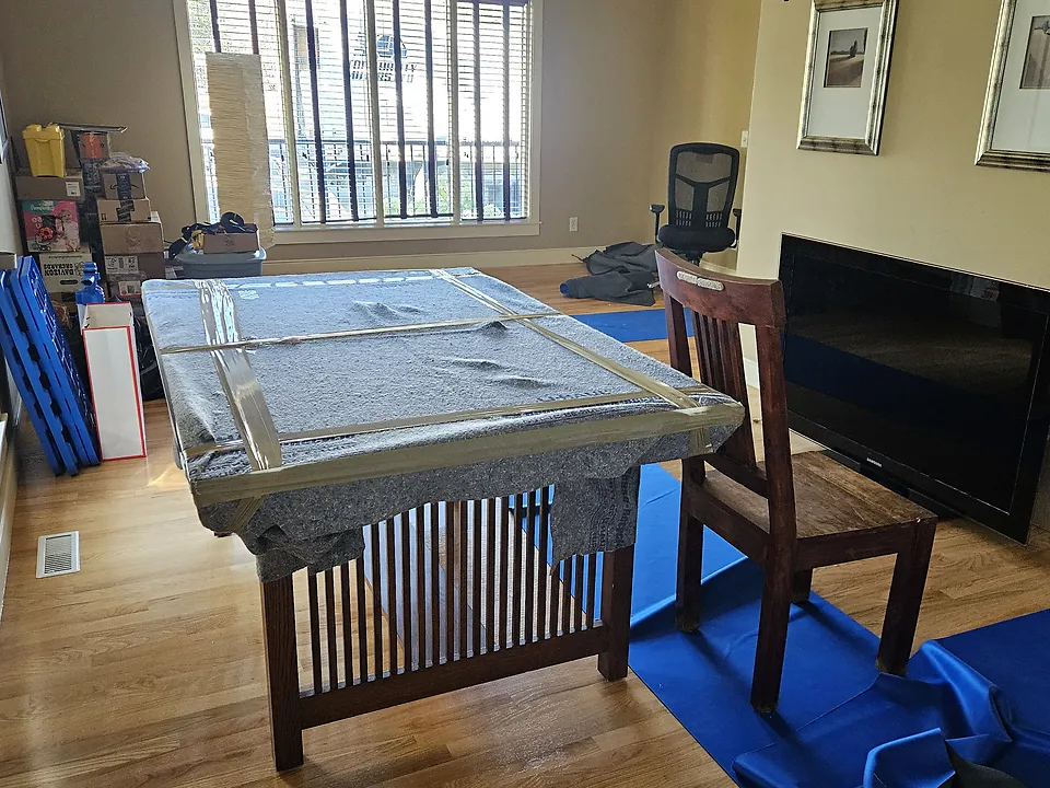 Dining table with its top padded in a moving blanket and taped, beside a blue floor runner