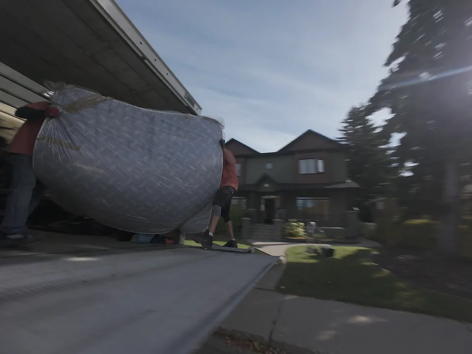Low drone view of two movers carrying a large wrapped piece out to the truck