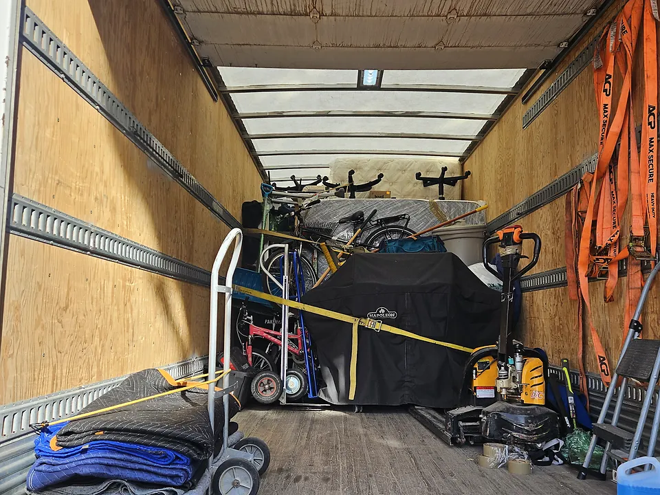 Bikes and a covered barbecue strapped in at the back of the truck's box, a hand truck and blankets by the door