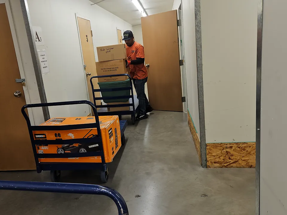 A mover with a loaded cart at a storage unit door in a storage facility hallway
