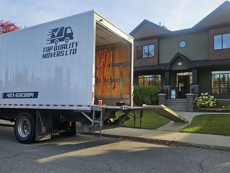 Branded moving truck at the curb with its ramp down, before loading begins at the house