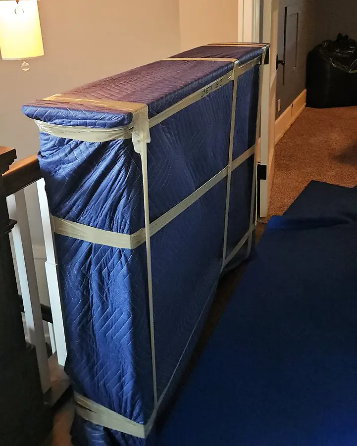 Tips for moving furniture: a piece wrapped in moving blankets and tape, on a floor runner at the top of the stairs