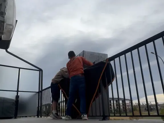 Two crew members at the balcony railing easing the couch over the side