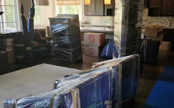 A sofa and furniture wrapped in moving blankets and shrink wrap on blue floor runners in a family home