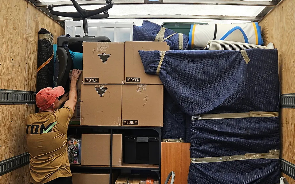 Inside our truck: boxes and blanket-wrapped furniture stacked in tiers up to the roof, with a crew member reaching up to the top tier