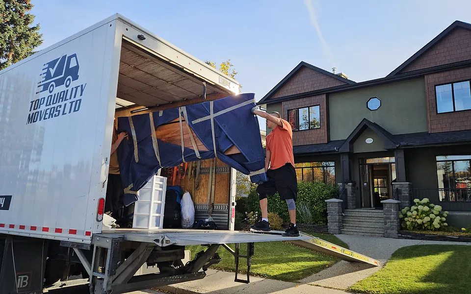 Our crew lifting blanket-wrapped furniture up the ramp into our truck outside a house in Hounsfield Heights, Calgary