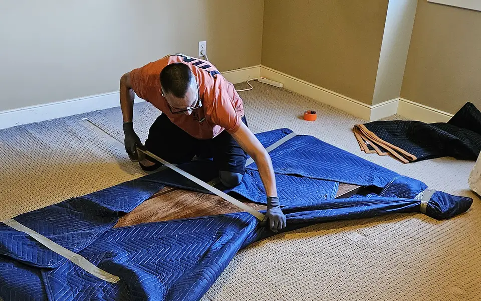 Residential movers in Calgary: our crew member tapes a moving blanket around a piece of furniture in an empty room
