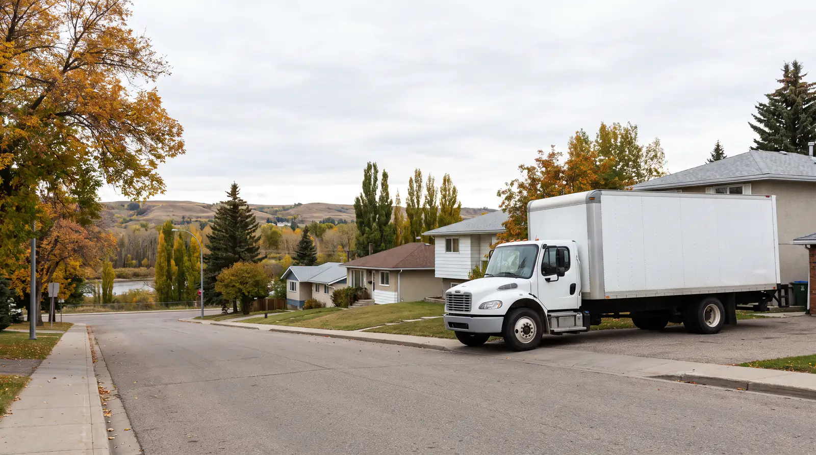 Movers in Okotoks: a plain white box truck parked on a residential street under autumn trees