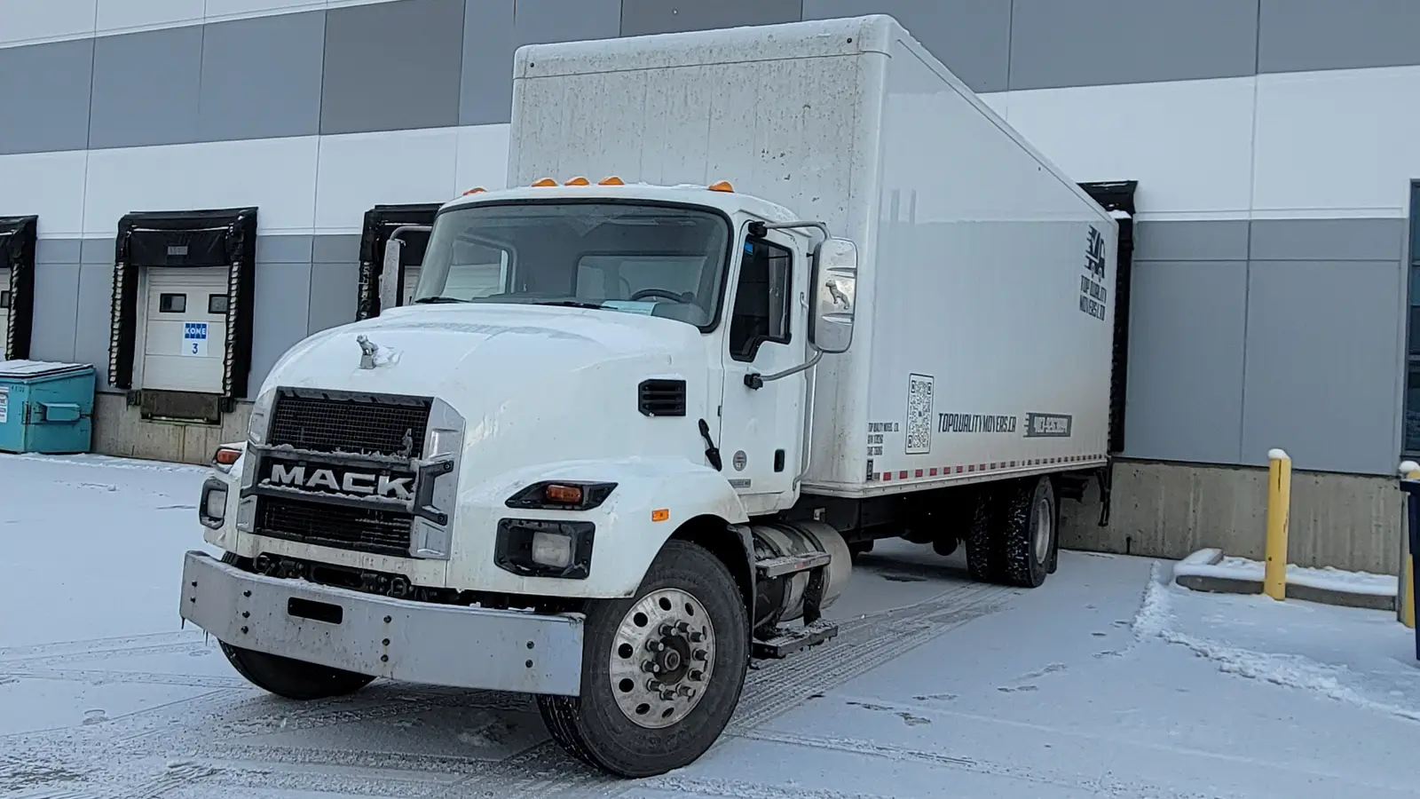 Hotshot services in Calgary: a white straight truck parked in the snow beside the loading docks of a warehouse