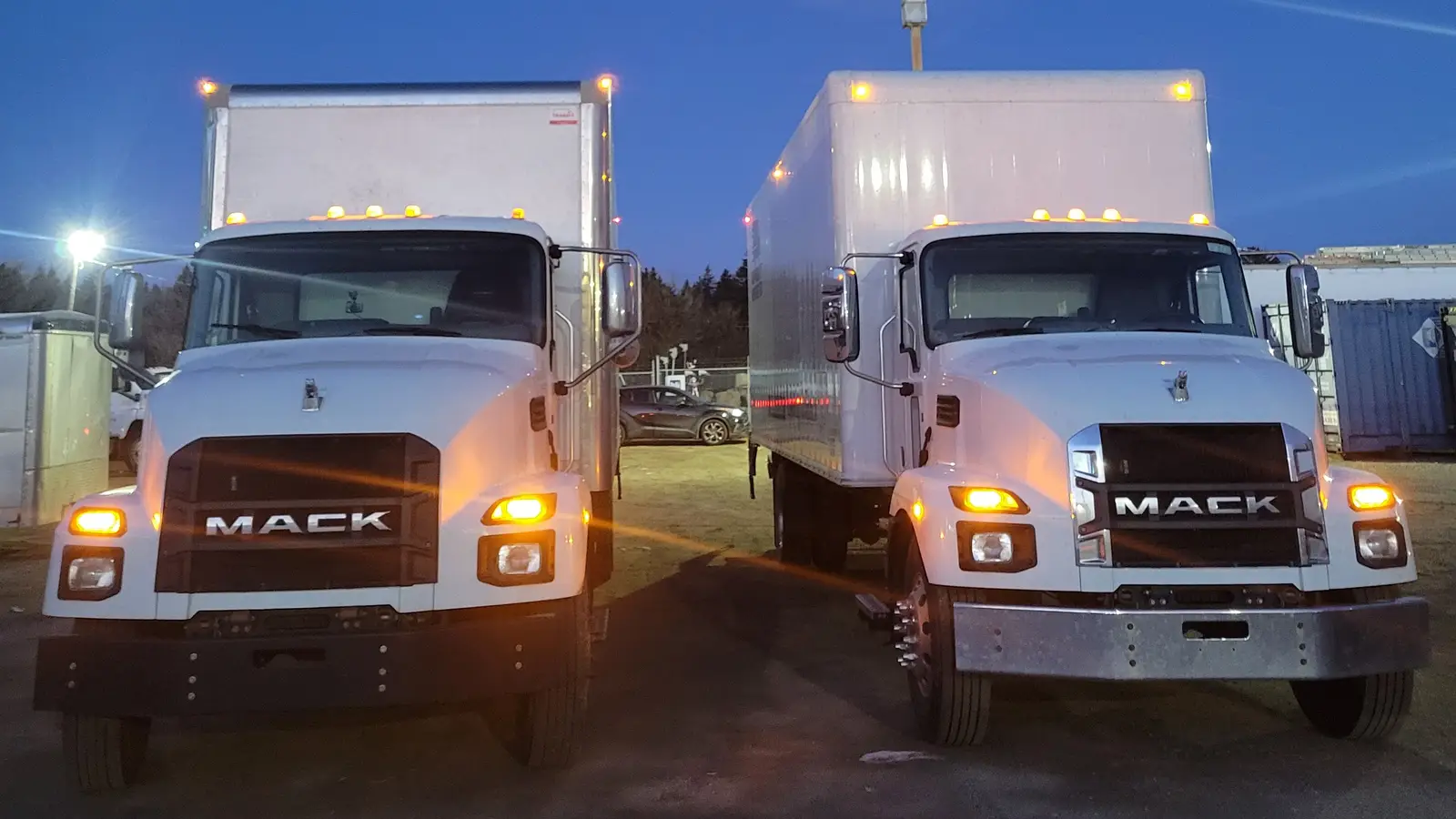 Transport company in Calgary: two white straight trucks with their headlights on, parked side by side at dawn